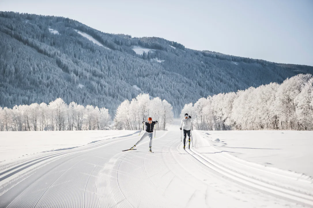 Zwei Personen beim Skilanglauf in einer verschneiten Landschaft 