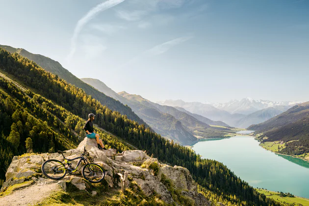 Eine Person mit dem Mountainbike blickt über den Reschensee im Vinschgau