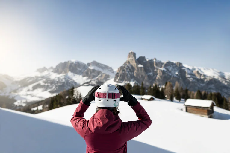 Eine Frau im Skianzug zieht sich die Skibrille über das Gesicht und blickt dabei auf die Dolomiten.