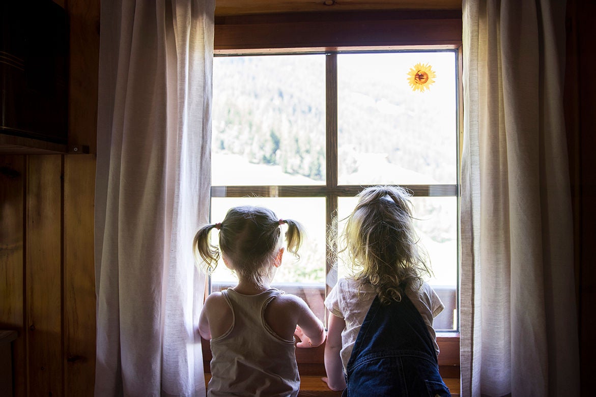 Zwei Kinder sitzen an einem Fenster in einer Ferienwohnung und schauen aus einem Fenster