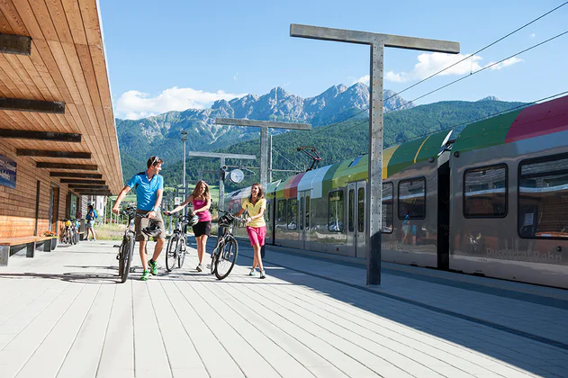 Three people next to a train, each pushing a bicycle next to them.