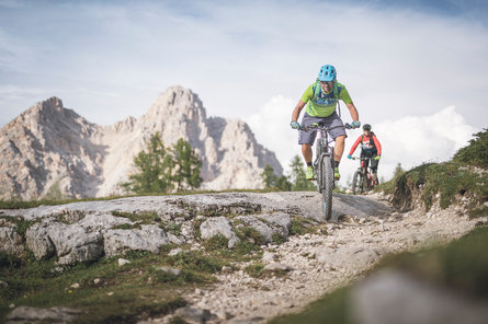 Due mountain biker su una strada di montagna, sullo sfondo prati, boschi e vette