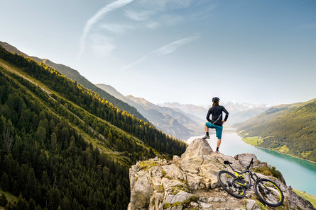 Cyklista na horském kole si dělá přestávku na hoře s výhledem na jezero Reschensee.