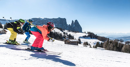 Zwei Kinder und eine erwachsene Person fahren auf Ski die Piste hinunter