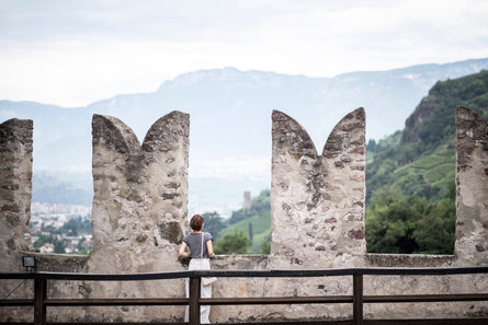 Una donna sul tetto di un castello ammira il paesaggio sulla e intorno alla città di Bolzano