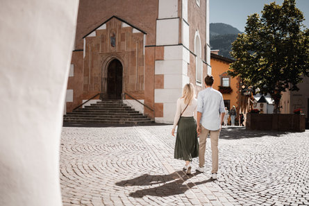 A couple stands in the sun in front of the old parish church in Kastelruth/Castelrotto.