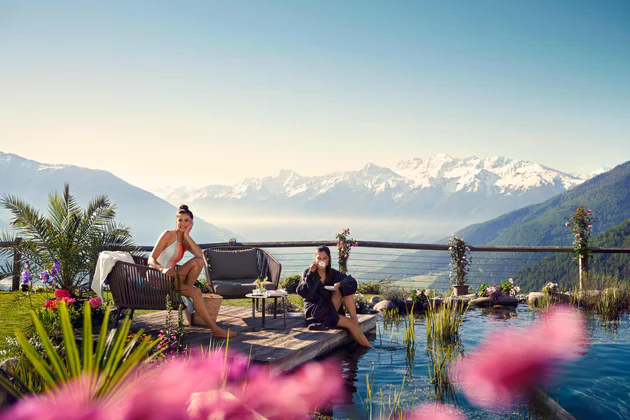 Dvě osoby relaxují u bazénu s horami v pozadí ve Vinschgau/Val Venosta
