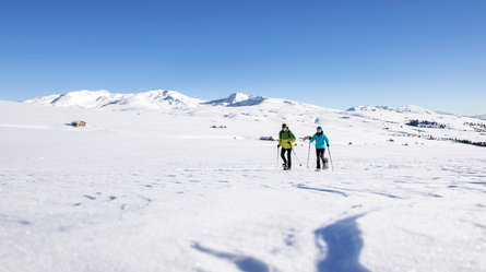 Ein Mann und eine Frau wandern mit Schneeschuhen über die schneebedeckte Villanderer Alm