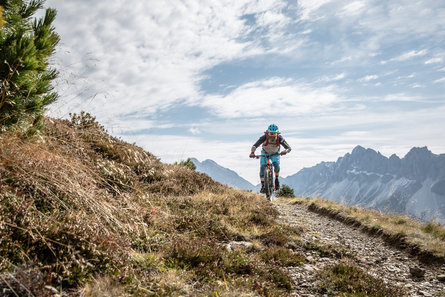 Een mountainbiker rijdt over een smalle weg, met op de achtergrond bergtoppen