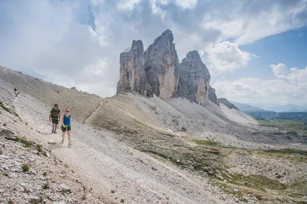 Una coppia di escursionisti in cammino, alle loro spalle svettano le Tre Cime di Lavaredo