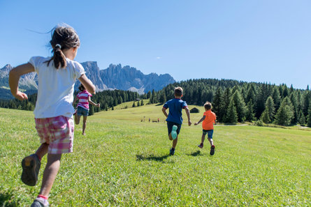 Bambini che corrono su un prato, con le Dolomiti in vista.