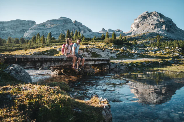 Dva přátelé sedí v létě na mostě přes potok u vesnice Al Plan / San Vigilio v Dolomitech