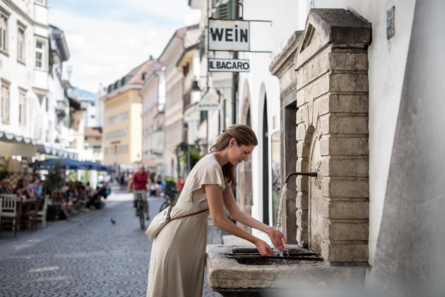 Una donna si rinfresca le mani presso una fontanella nel centro storico della città di Bolzano