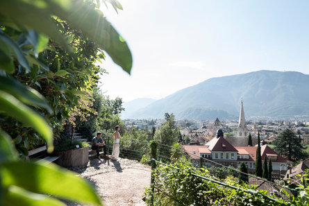 A couple takes a moment to rest and enjoy the view over the city of Bolzano during a walk on the panoramic Guntschnapromenade