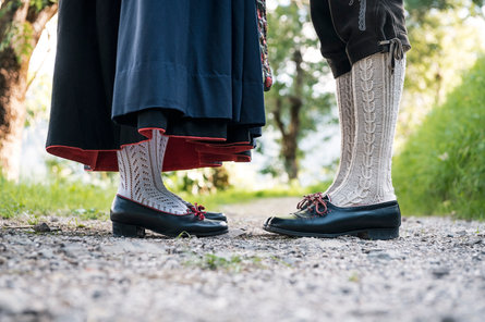 The legs and feet of a man and a woman wearing traditional footwear as well as classic South Tyrolean stockings and traditional Tracht clothing.