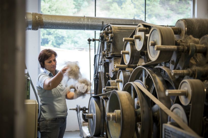 Eine Frau sortiert nebe einer großen Maschine auf traditionelle Art Wolle.