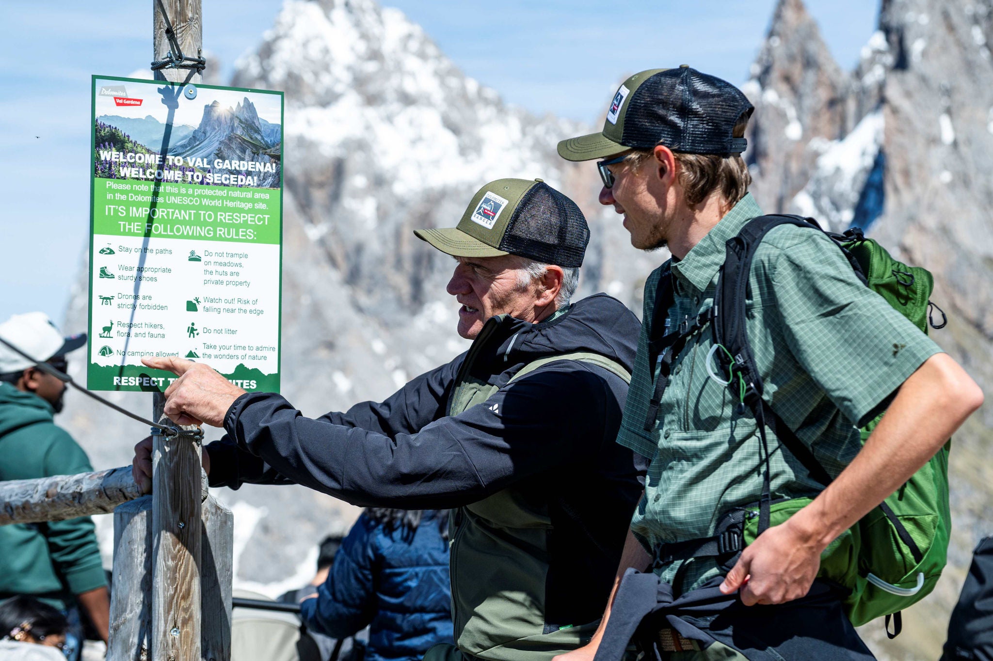 Zwei Dolomiten-Ranger zeigen ein Schild mit Verhaltenshinweisen im Grödner Tal.