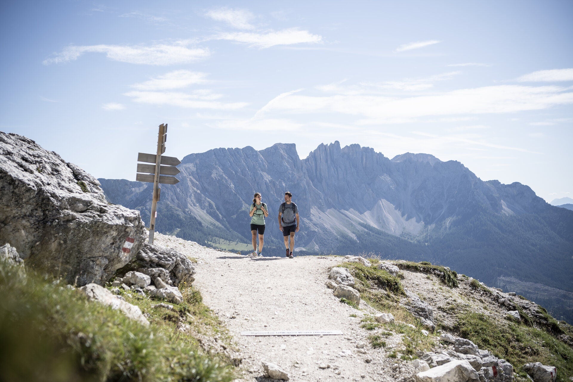 Ein Mann und eine Frau wandern auf einem Weg, hinter ihnen erhebt sich die Bergformation Latemar
