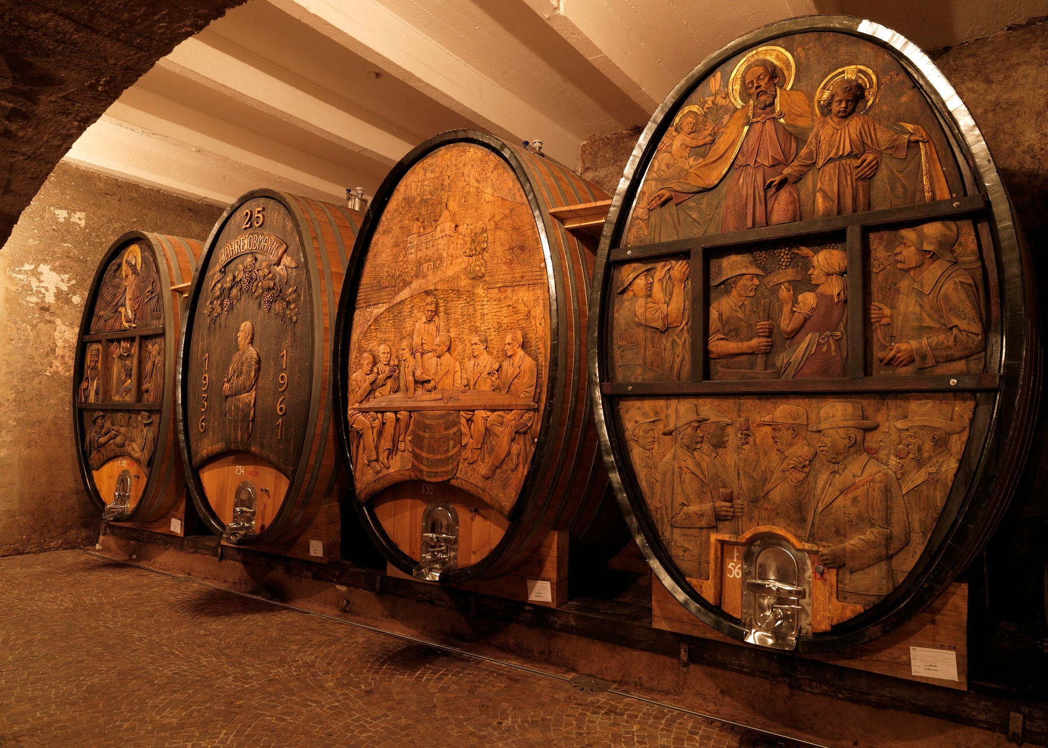 Vier kunstvoll mit profanen und sakralen Motiven gestaltete historische Weinfässer stehen nebeneinander im Keller.