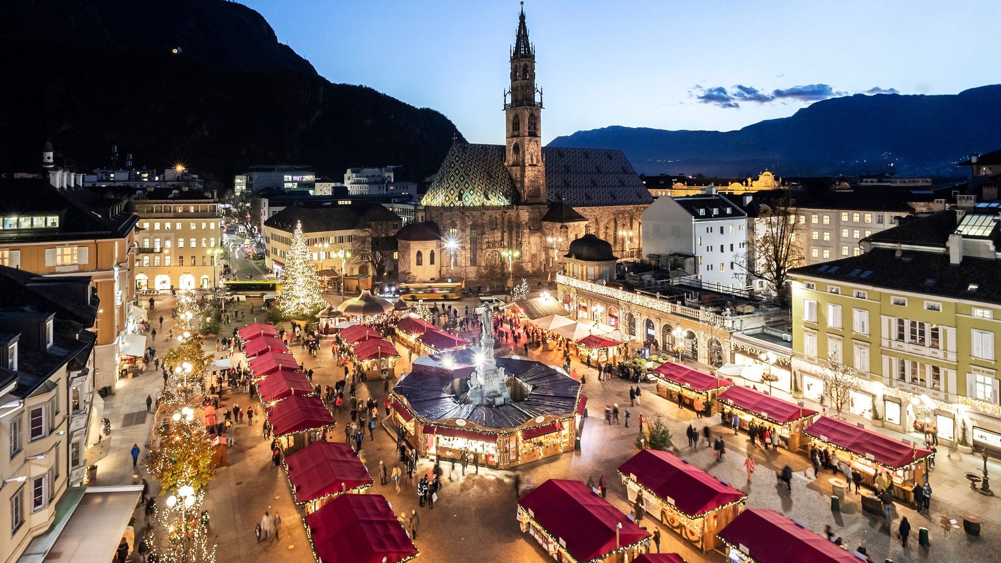 Die roten Dächer der Stände des Bozener Weihnachtsmarkts vor dem Dom und einem strahlend blauen Himmel.