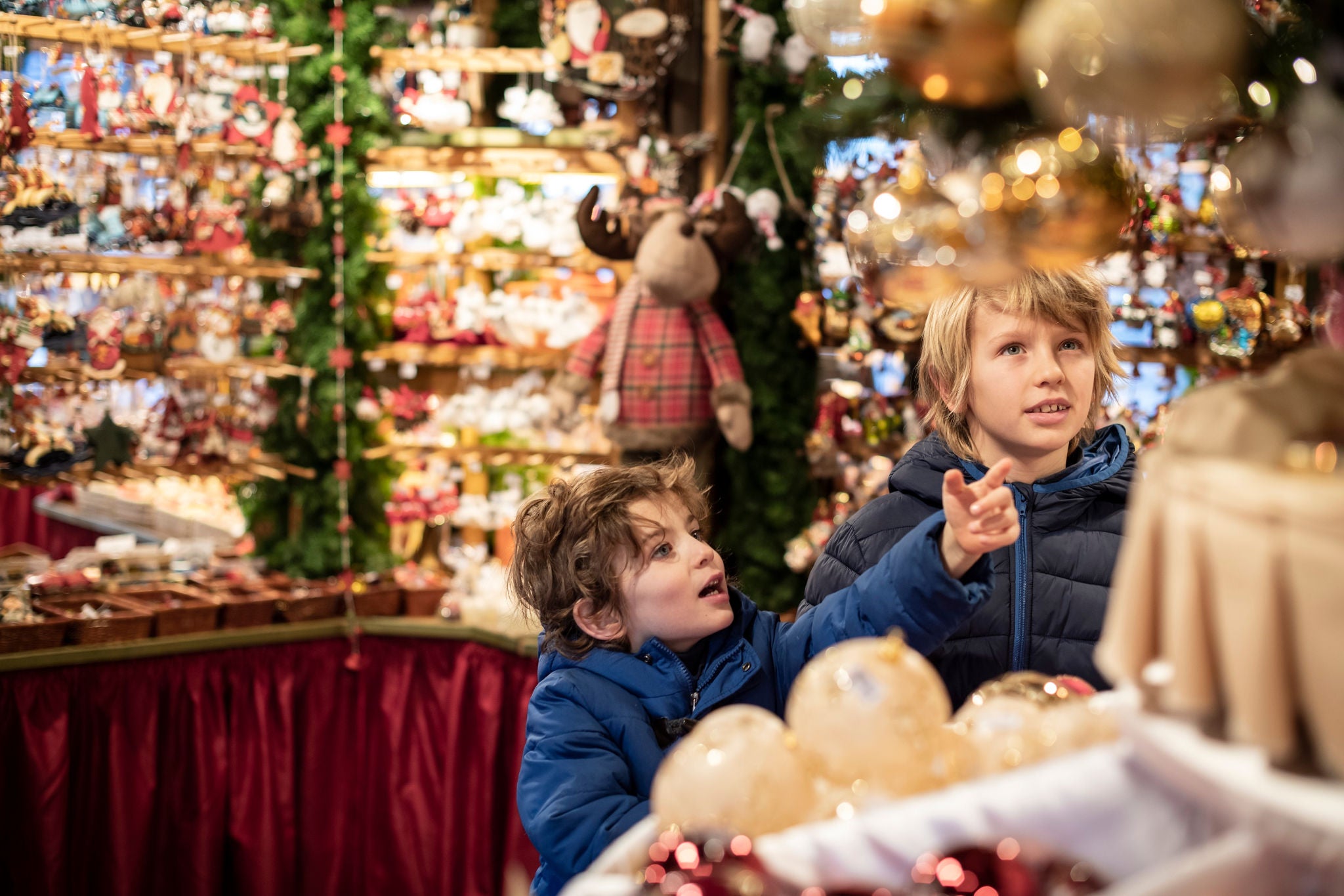 Zwei Kinder bestaunen auf dem Christkindlemarkt in Bozen angebotene Weihnachtswaren.
