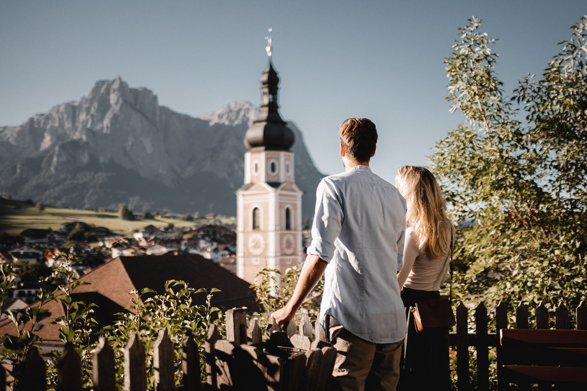 Ein Mann und eine Frau stehen am Zaun und genießen die Aussicht auf Kastelruth mit seinem schönen Kirchtum.