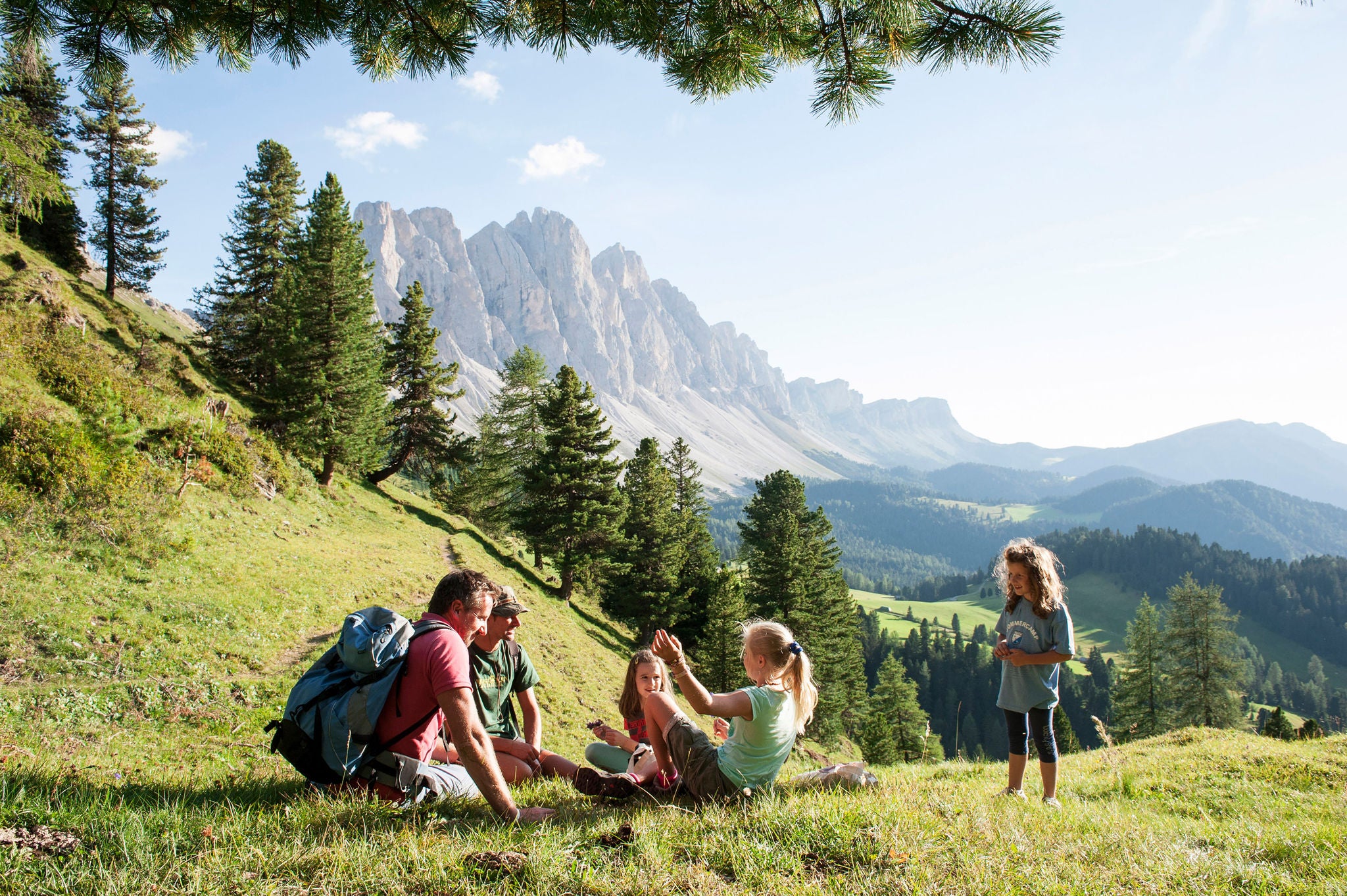 Eine Familie sitzt auf einer Wiese  mit einem Tal im Hintegrund im Sommer