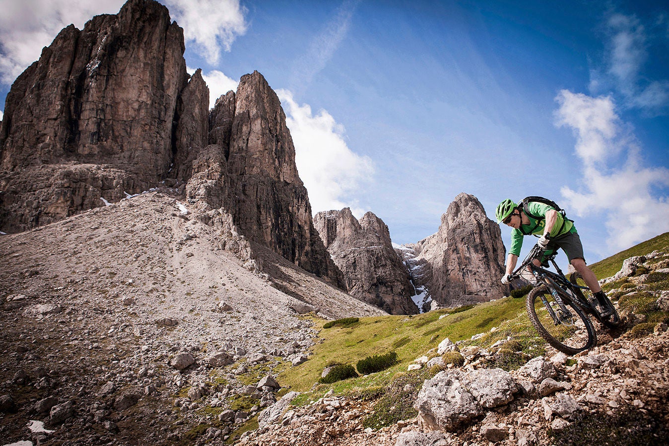 Mountainbiker auf einem steinigen Trail, dahinter erheben sich zackige Bergspitzen