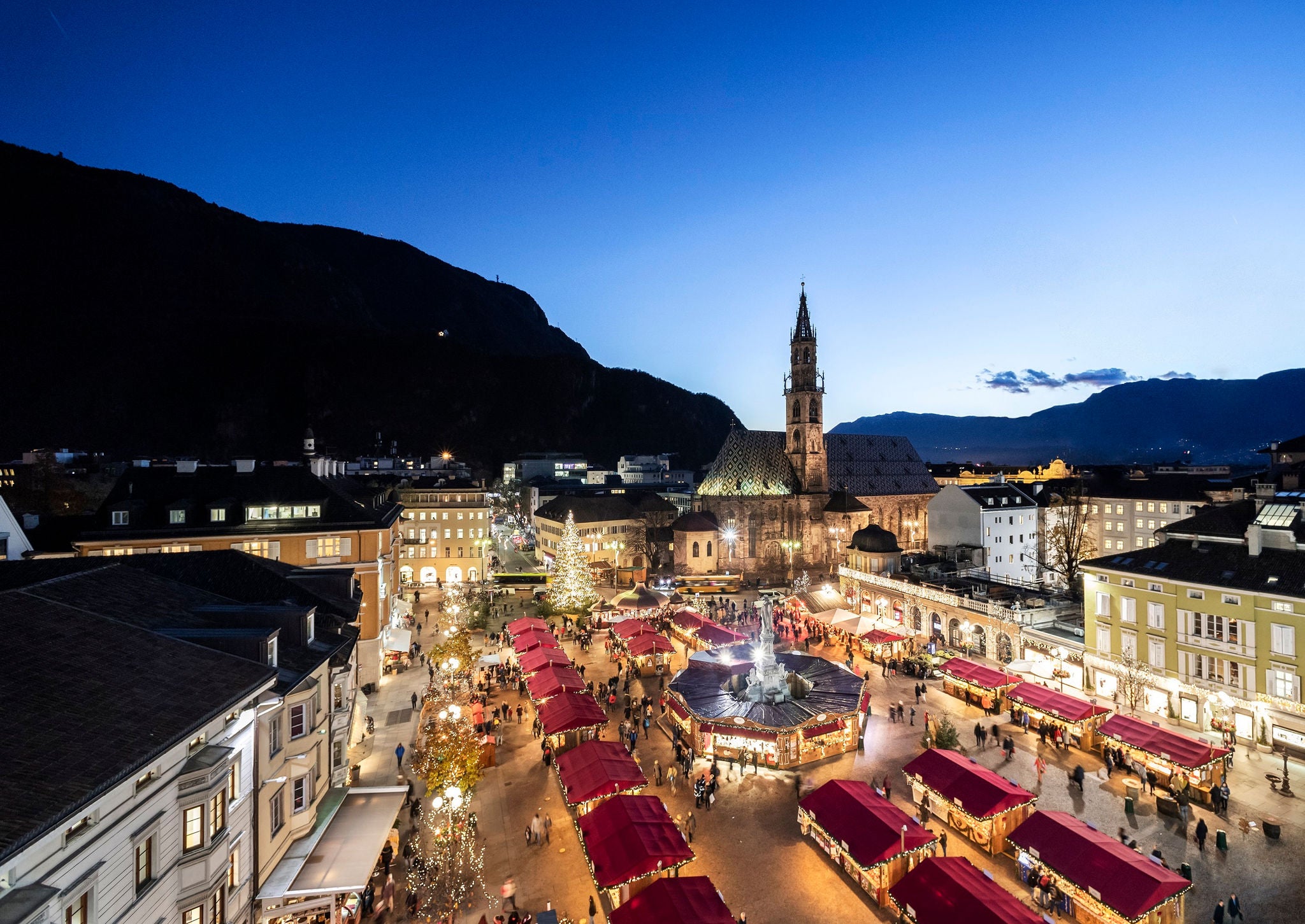 Die roten Dächer der Stände des Bozener Weihnachtsmarkts vor dem Dom und einem strahlend blauen Himmel.