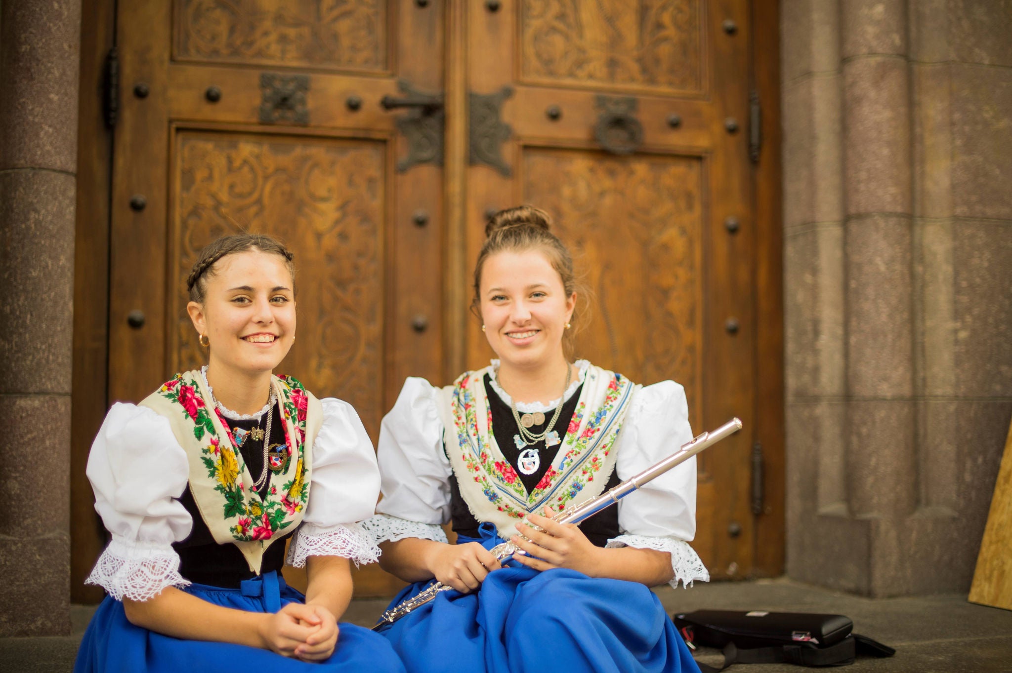 2 Mädchen in Tracht sitzen vor einer Kirche in Meran