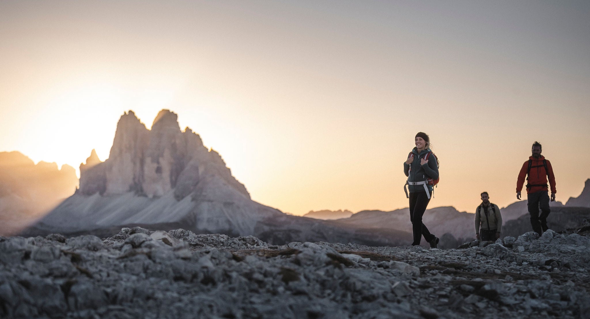 Zwei Manner und eine Frau wandern im Hochgebirge, wÃ¤hrend die Sonne hinter den Dolomiten versinkt