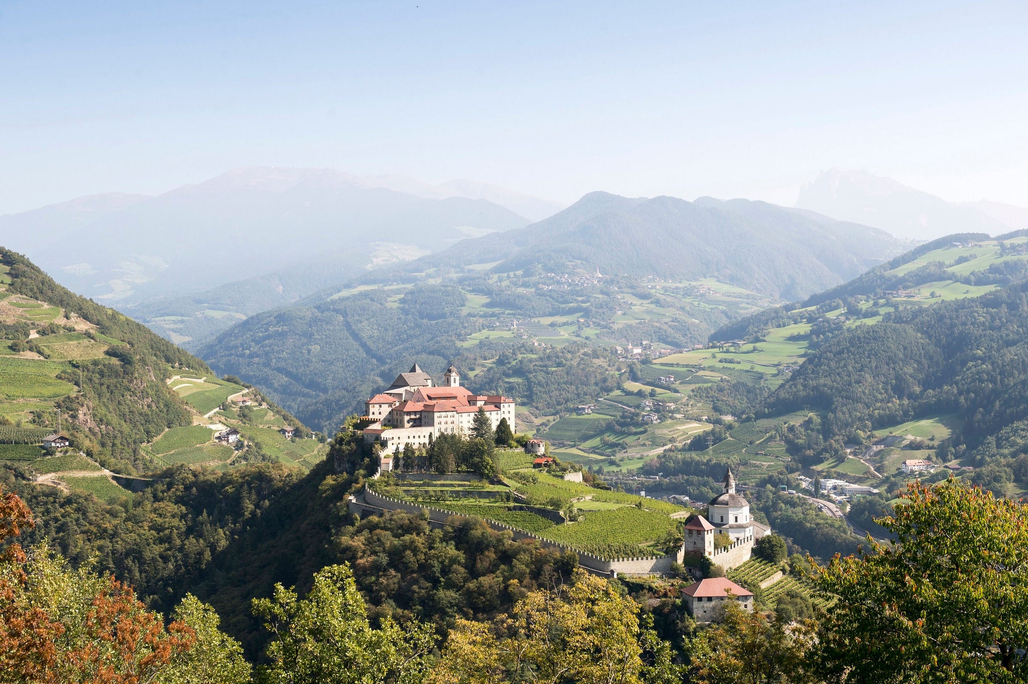 Kloster Säben oberhalb von Klausen inmitten der Weinhänge und die Berge im Hintergrund