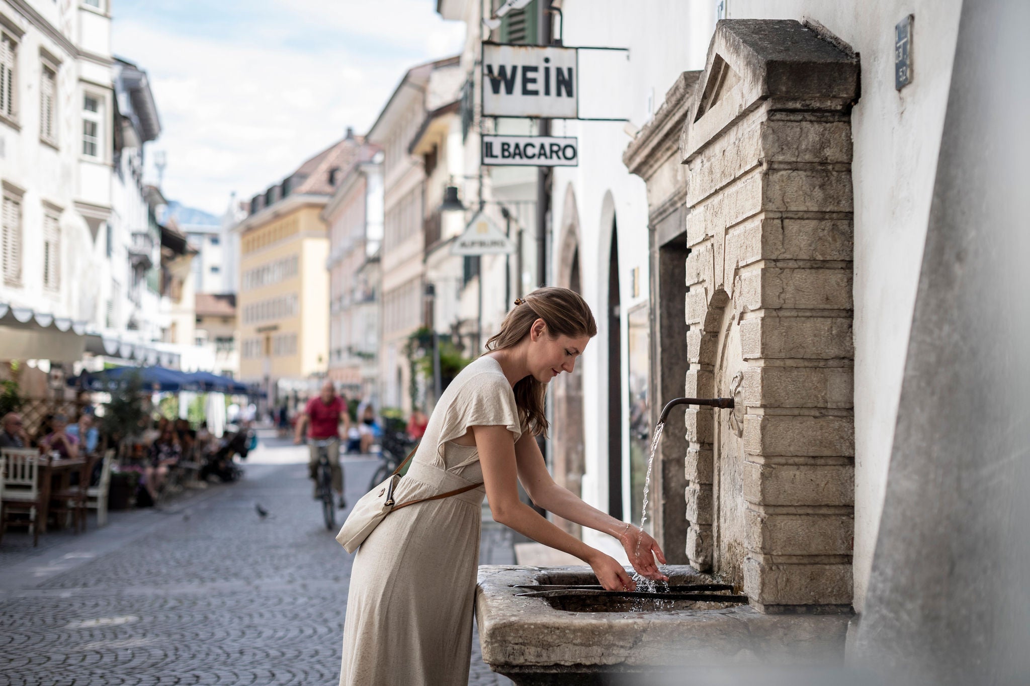 Frau erfrischt sich an einem Brunnen bei einem Stadtbummel durch Bozen
