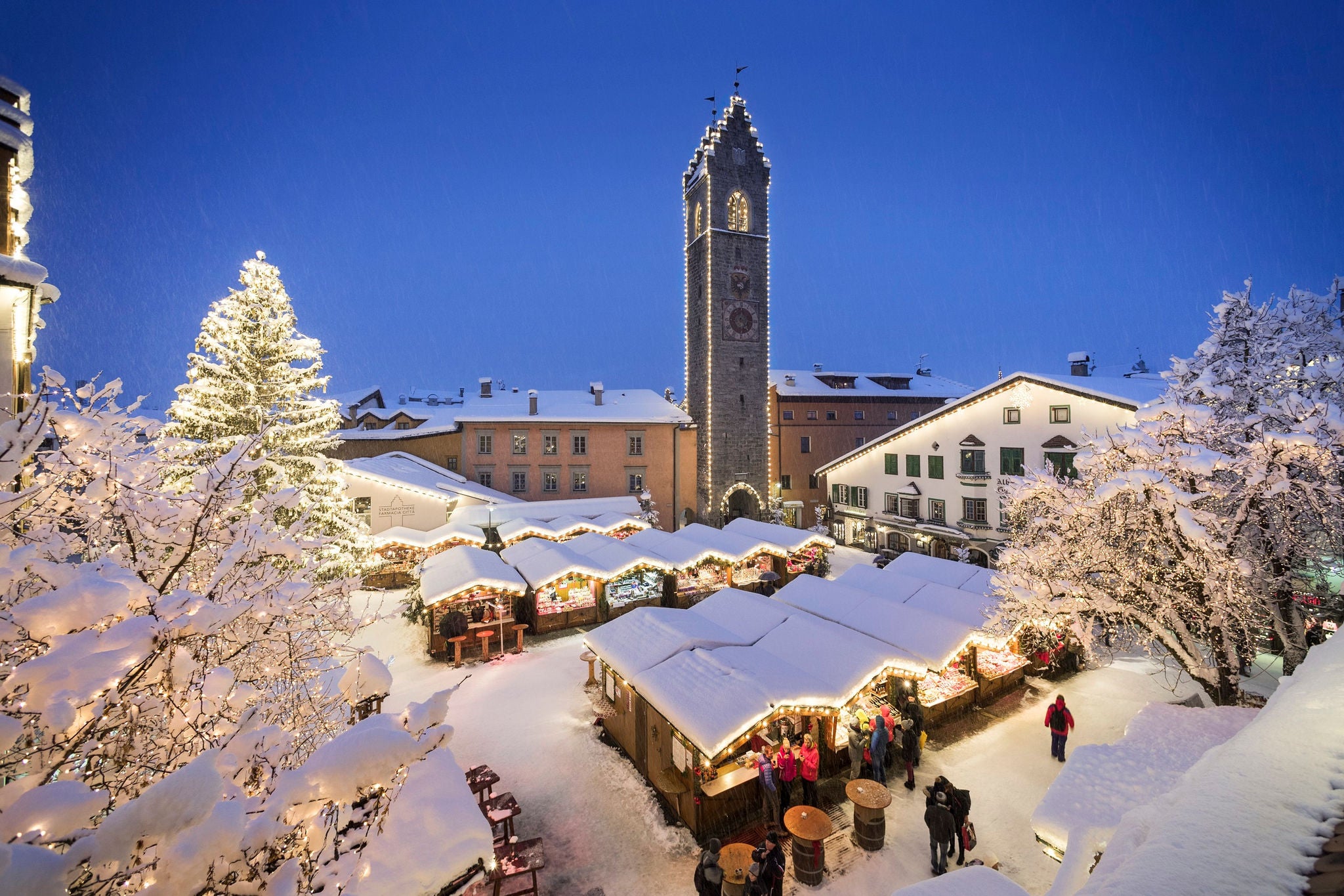 Schneebedeckte Hütten auf dem Christkindlmarkt in Sterzing vor dem Zwölferturm.