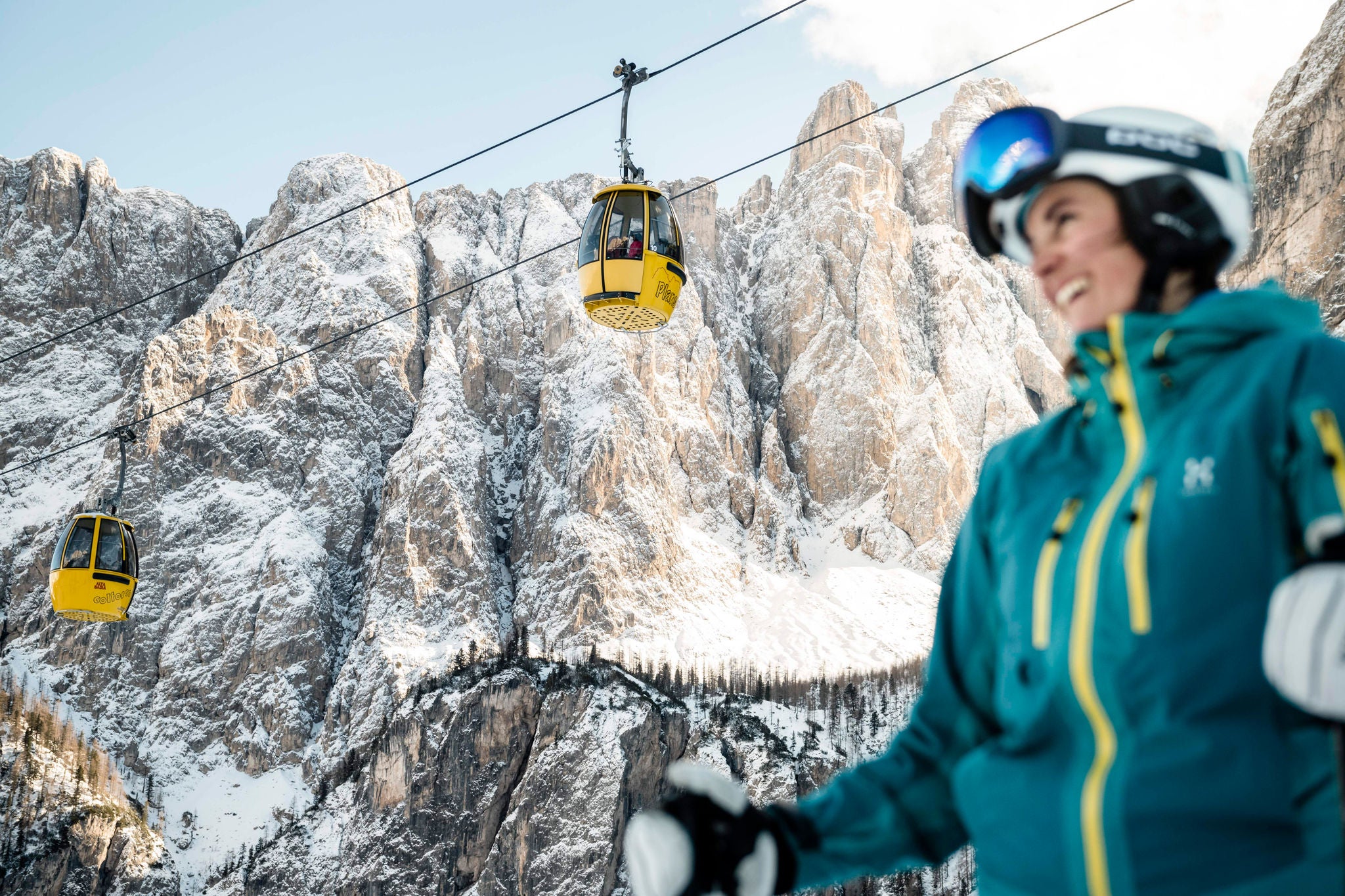 Eine lachende Frau in Skikleidung vor zwei Gondeln der Sella-Ronda-Seilbahn.