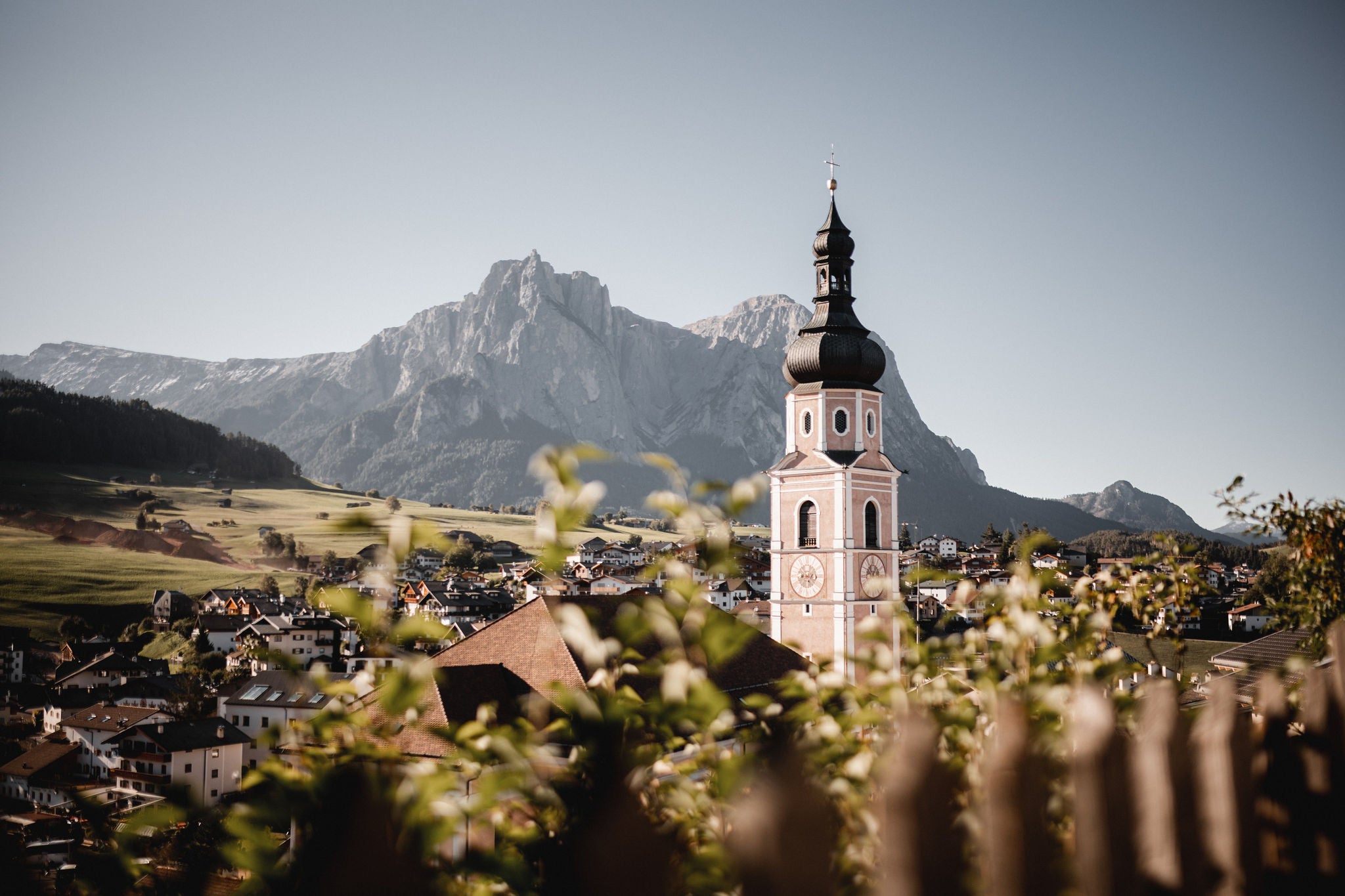 Blick auf den Kirchturm von Kastelruth mit Bergpanorama im Hintergrund an einem schönen Sommertag