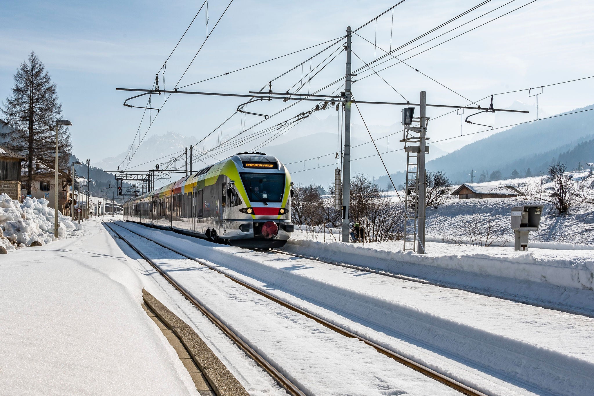 Ein Regionalzug fährt durch eine schneebedeckte Winterlandschaft in Südtirol.