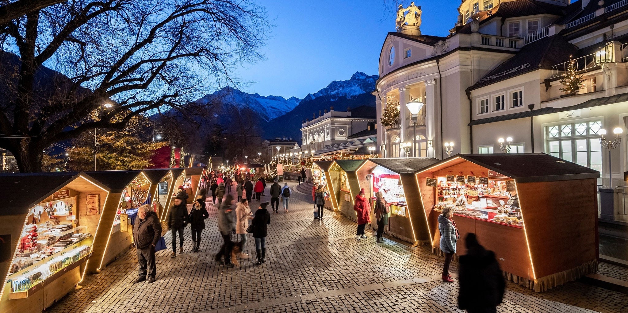 Die beleuchteten Buden des Meraner Weihnachtsmarktes vor einem klaren, blauen Abendhimmel.