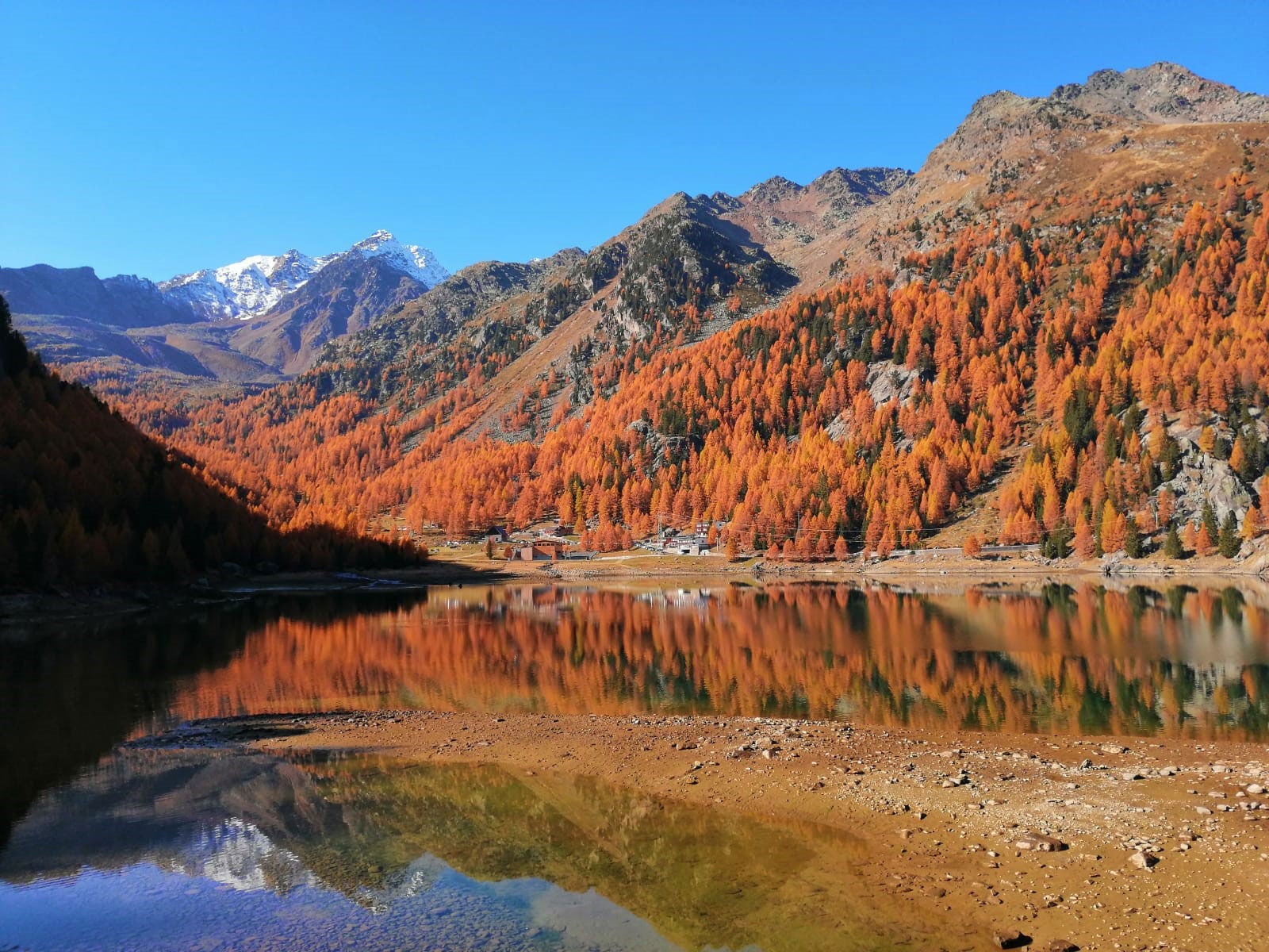 ein See mit Bäumen und Bergen im Hintergrund bei Ultental im Herbst