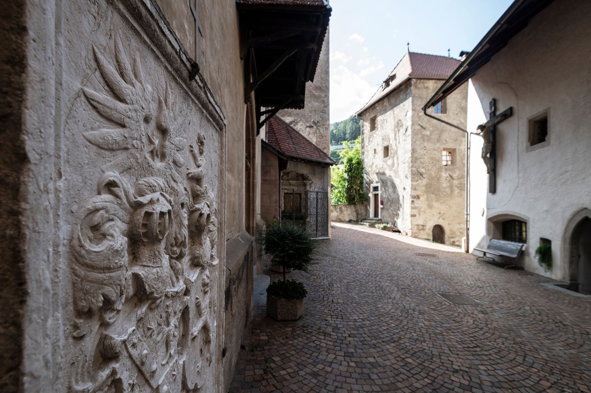 In Stein gemeiseltes Ritterwappen an der Fassade der Pfarrkirche, gegenüber hängt ein großes Kreuz auf der Hauswand