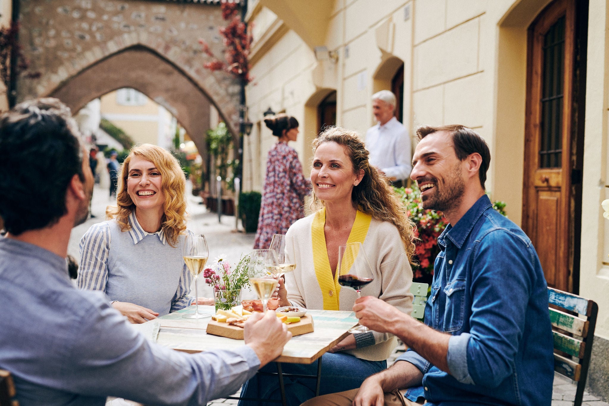 Zwei Frauen und zwei Männer lächeln und genießen draußen einen Aperitiv in der Altstadt von Bozen.