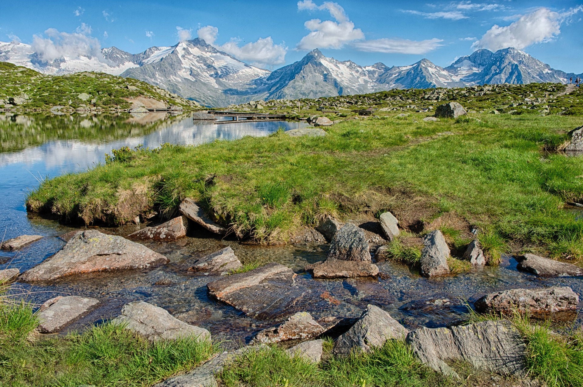 Ein Bergbach schlängelt sich durch eine Almwiese vor imposanter Bergkulisse