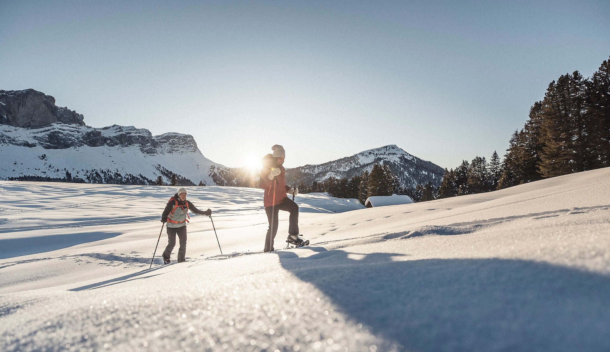 Die Sonne lässt den Schnee glitzern, auf dem zwei Schneeschuhwanderer bergauf laufen.