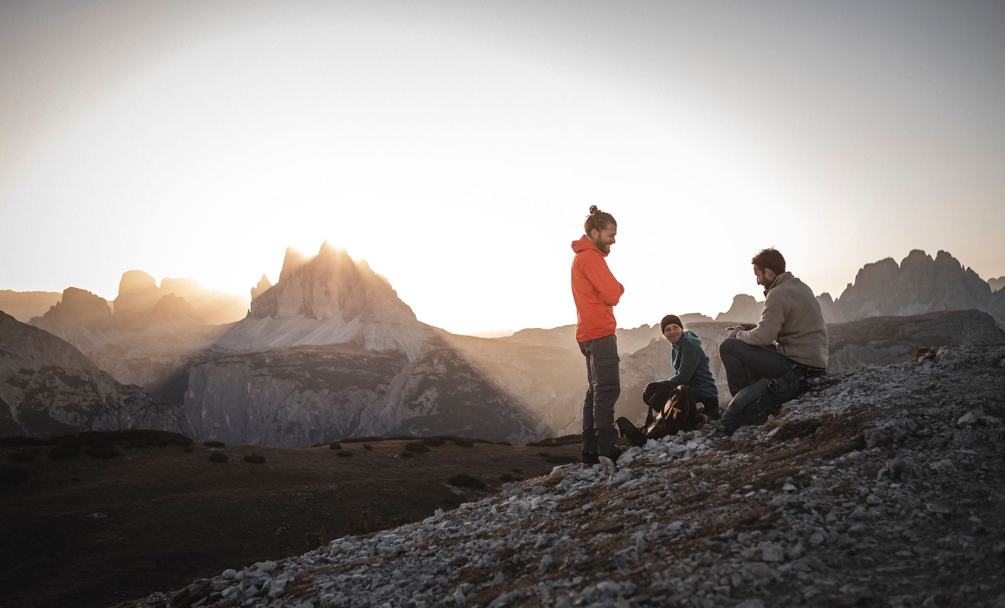 Zwei MÃ¤nner und eine Frau bei einer kurzen im Gebirge mit Blick auf die Drei Zinnen Bergformation im Morgenlicht