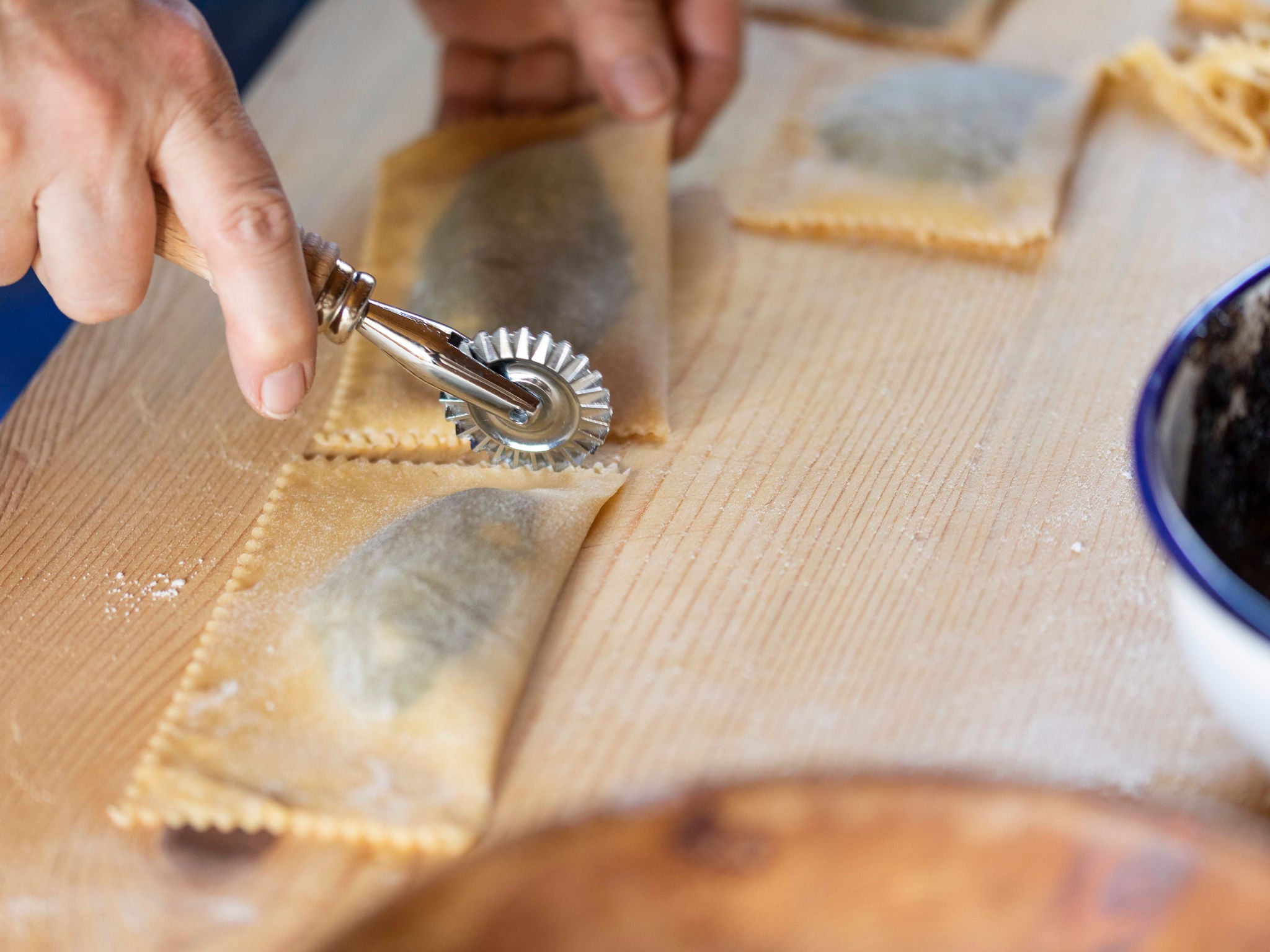 Auf einer Arbeitsplatte aus Holz bekommen die typischen Bauernkrapfen ihre eckigen Ränder durch das Rollen mit dem Teigroller.