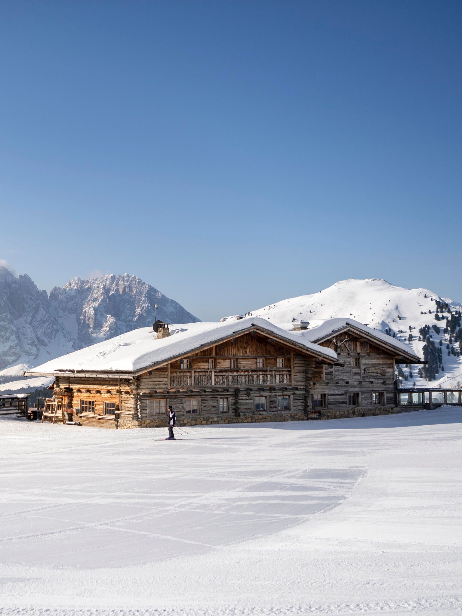 Eine Skihütte im Vordergrund, mit einem verschneiten Panorama um sie herum