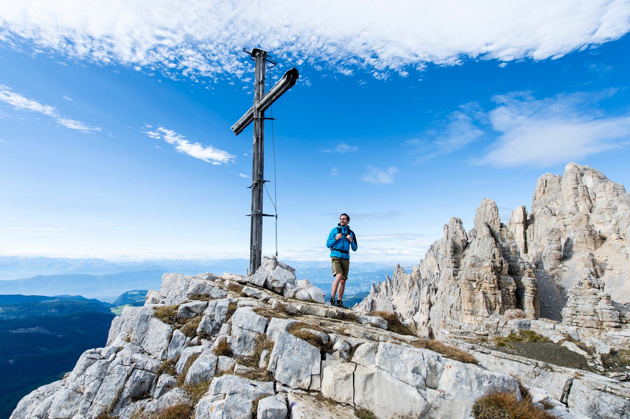 Ein Wanderer lächelt bei seiner Ankunft auf dem Gipfelkreuz auf dem Latemar inmitten der Dolomiten