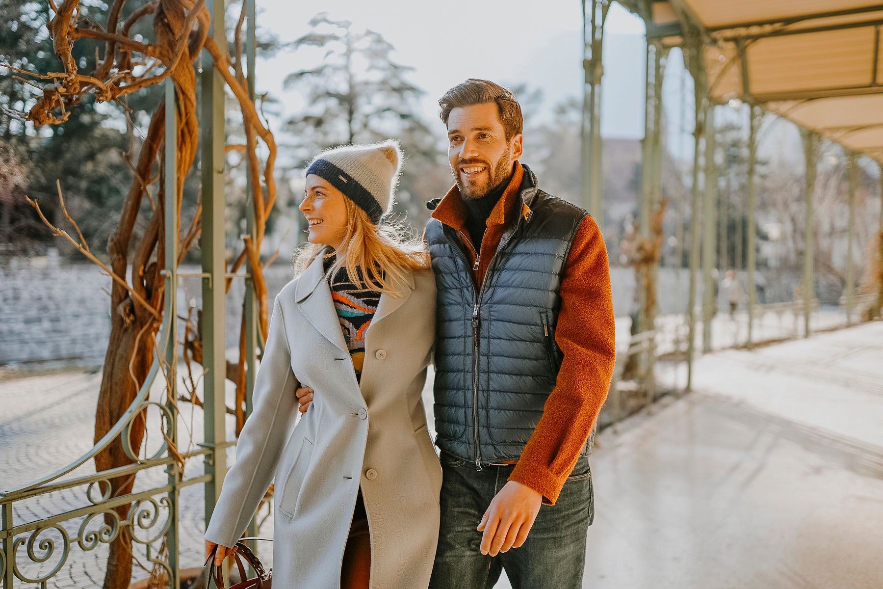 Eine Frau und ein Mann flanieren im Winter vor der historischen Wandelhalle durch Meran.