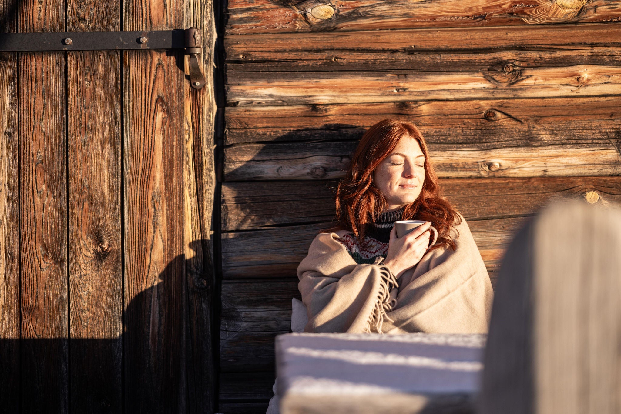 Eine Frau geniesst die Wintersonne vor einer Hütte auf der Seiser Alm 