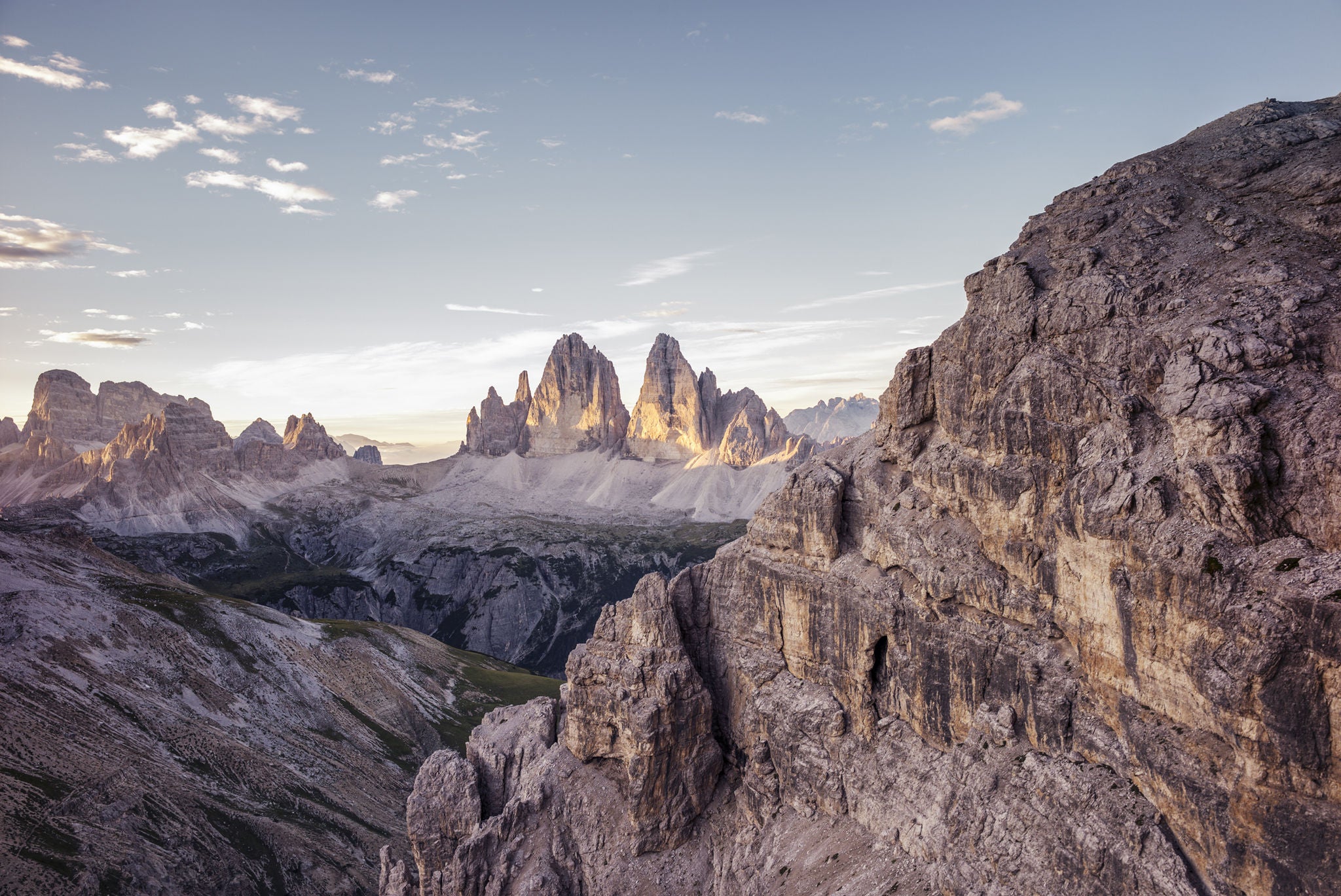 Blick auf das Bergpanorama der Dolomiten mit der majestätischen Formation der Drei Zinnen in der Bildmitte, von Sonne beschienen. 